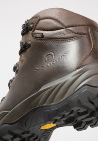 Brune lærstøvle til vandreture med en tekstureret overflade, udstyret med sort hardware og en Vibram sål. Vandtæt Gore-Tex-mærke synligt.