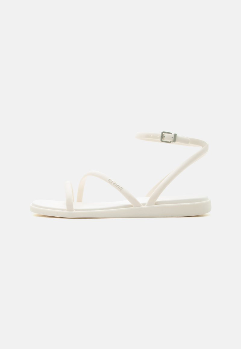 Sandale plate blanche avec fines lanières, boucle à la cheville et orteil ouvert, présentée de profil sur un fond uni.