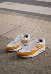 Weiße und orange Nike Air Max Sneakers mit einem Obermaterial aus Wildleder und Mesh, runder Zehenpartie, flachen Schnürsenkeln und sichtbarer Luftpolsterung in der Ferse.