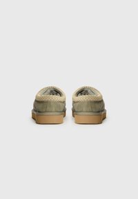 Scarpe in suede verde con un bordo intrecciato beige, parte posteriore rotonda e suola piatta in gomma. La finitura texturizzata e il design semplice le rendono versatili.