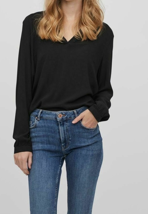 Maglietta nera a maniche lunghe con scollatura a V, abbinata a jeans in denim blu con chiusura a bottoni e tasche frontali.