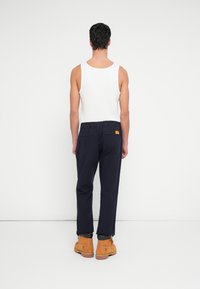 Biała bezrękawnikowa koszulka i granatowe spodnie z elastycznym pasem oraz tylnymi kieszeniami. Brązowe buty z czarnymi podeszwami i detalami przeszyć.