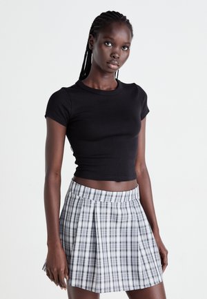 Zwarte fitted crop top gecombineerd met een geplooide minirok met een zwart-wit ruitpatroon. Model staat tegen een neutrale achtergrond.