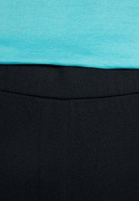 T-shirt en coton turquoise superposé sur un pantalon en tissu extensible noir, présentant une texture lisse et un design ajusté à la taille.