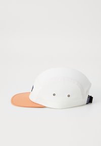 White cap with an orange brim, featuring metal ventilation eyelets and an adjustable strap on the back. Flat peak design.