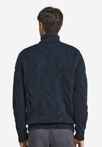 Mörk marinblå tröja med hög ribbad krage. Har texturerade mönster samt ribbade ärmslut och nederkant. Tillverkad av ett tjockt stickat material.