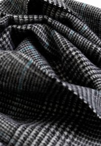 Tela de lana tejida con un patrón de pata de gallo en negro y gris, acentuada con delgadas líneas azules, textura suave y apariencia arrugada.