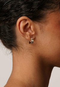 Guldörhänge med en böjd design, prytt med klara rhinestones längs den främre kanten. Slät, glänsande yta, lätt och luftig känsla.