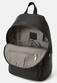 Sac à dos en cuir noir avec une forme arrondie, intérieur gris, poche zippée à l'avant et une poignée supérieure pour un transport facile.