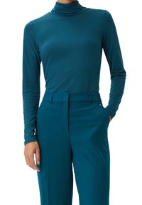 Türkises Rollkragenoberteil mit langen Ärmeln, aus glattem Stoff gefertigt. Kombiniert mit türkisfarbenen, hoch sitzenden Hosen mit taillierter Passform und vorderen Taschen.