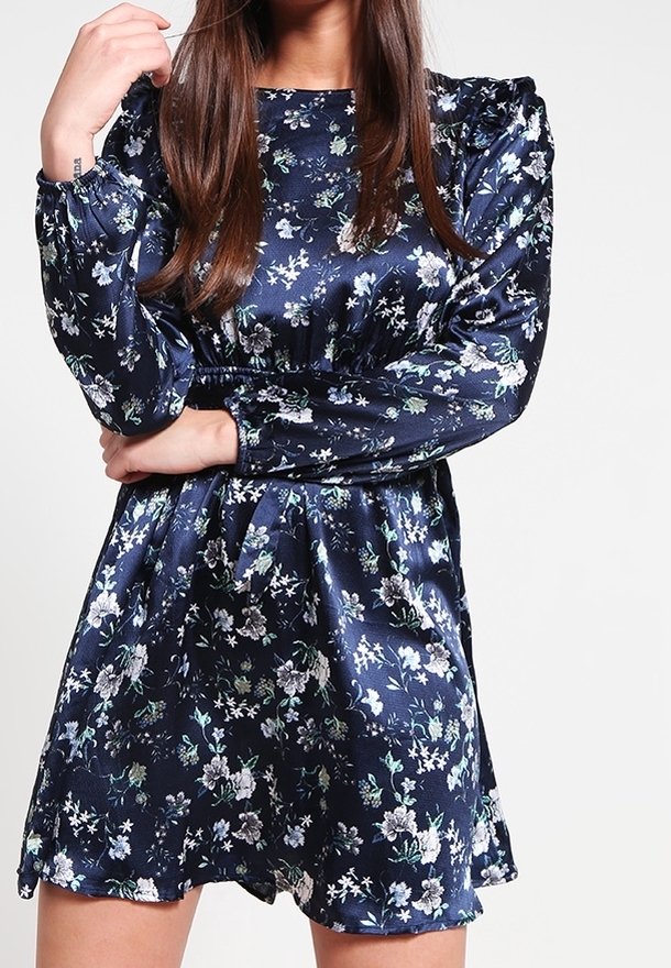 Robe florale bleu marine en satin avec des manches bouffantes, une taille froncée et une jupe évasée ; présente des motifs floraux blancs et verts.