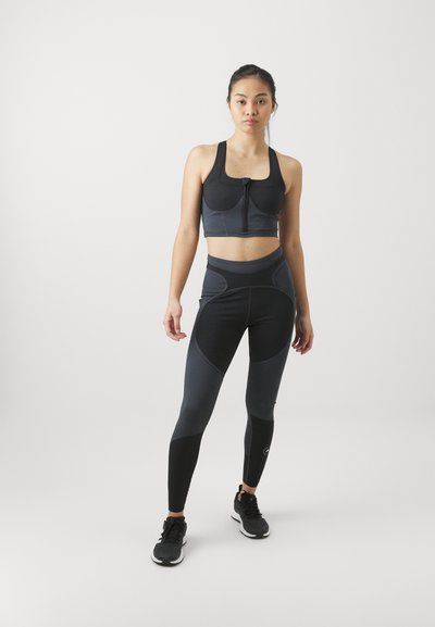 Svart sports-bh med frontlås, parret med højtaljede leggings i varierende grånuancer. Har en glat tekstur og atletisk design.