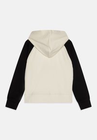 Felpa con cappuccio caratterizzata da un corpo crema e maniche raglan nere. Materiale in cotone, polsini e orlo a coste, e una tasca frontale.