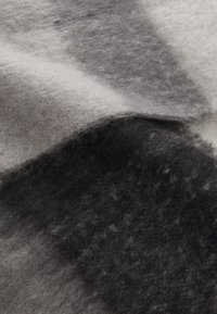 Tecido de lã cinza e preto com uma textura suave e felpuda, apresentando um padrão de degradé de tons claros a escuros, dobrado sobre si mesmo.