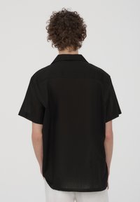 Camisetta nera a maniche corte con vestibilità morbida, colletto e tessuto testurizzato. La camicia presenta un orlo dritto e dettagli minimi.