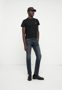 Svart bomullst-skjorte med en liten logo, mørkeblå denim jeans og svarte skinnloafers, komplementert med en svart caps.