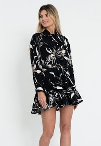 Abito nero con maniche lunghe, caratterizzato da un motivo floreale e astratto in tonalità di bianco e beige. Ha una vita aderente e una gonna svasata.