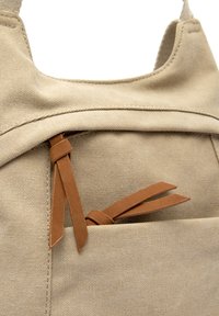 Beżowy plecak z płótna z kieszenią na zamek, wyposażony w dwa brązowe skórzane uchwyty oraz szczegółowe przeszycia.