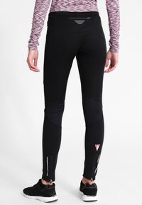 Schwarze Sportleggings mit reflektierenden Akzenten, Reißverschlussbündchen und strukturiertem Bund. Hergestellt aus dehnbarem, feuchtigkeitsableitendem Material.