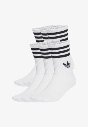 Calcetines deportivos blancos con tres rayas negras horizontales en la parte superior, textura acanalada y un logo negro en el lateral. Conjunto de tres pares.