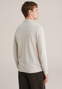 Pletený pulóver v svetlo béžovej farbe s textúrovanou látkou, ktorý má pásikový golier, manžety a lem. Dizajn je priliehavý a jednoduchý.