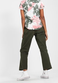 Lyhythihainen paita, jossa on vaaleanpunaisia ja vihreitä kukkakuvioita valkoisella taustalla, yhdistettynä oliivinvihreisiin housuihin ja valkoisiin korkeisiin tennareihin.