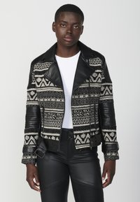 Giacca a strisce bianco e nero con dettagli in pelle, caratterizzata da un colletto a risvolto e una chiusura con zip; tessuto testurizzato con design geometrici.