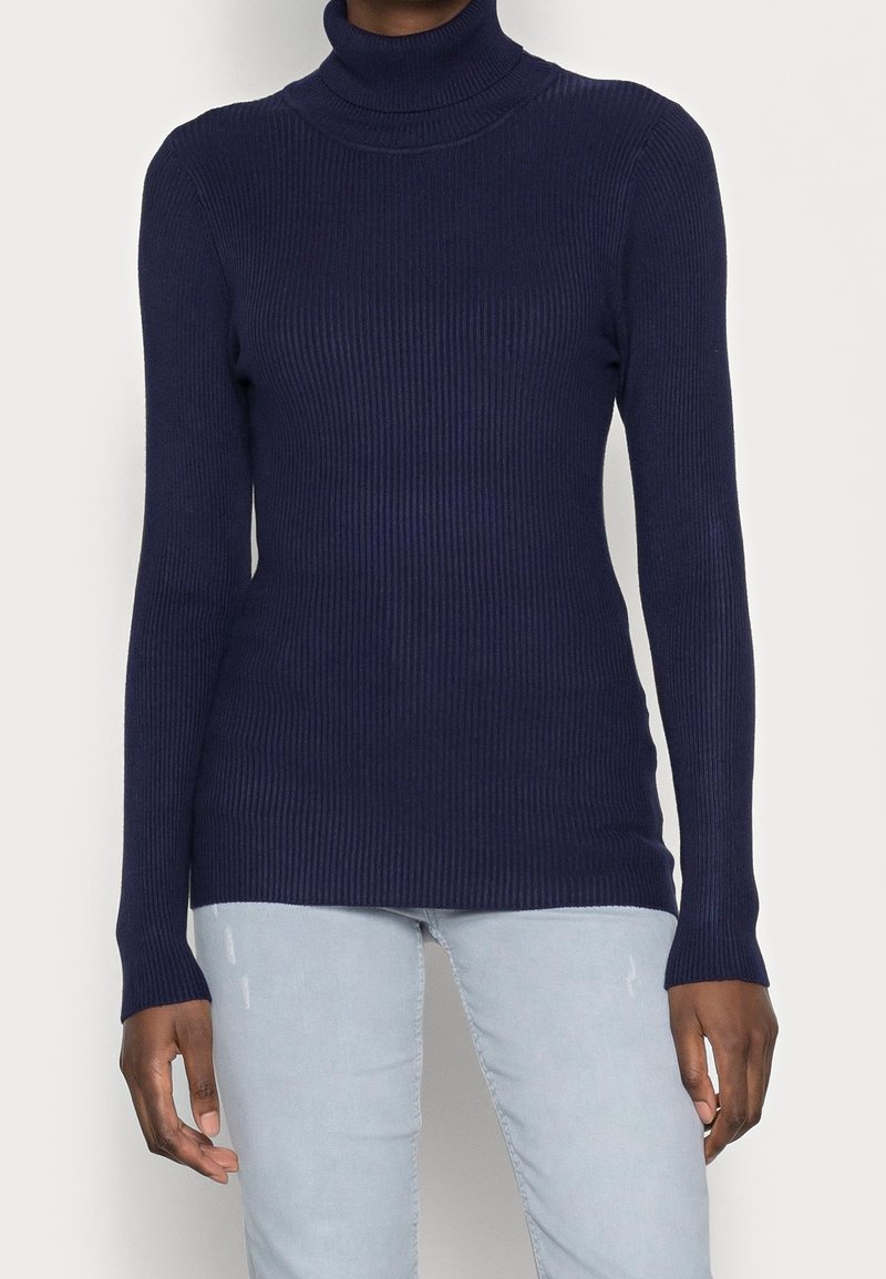 Pull à col roulé côtelé bleu marine avec manches longues et silhouette ajustée, confectionné en matière douce et extensible.