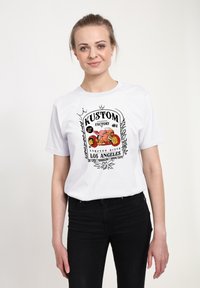Hvid t-shirt med et sort grafikprint, der viser et motorsydesign og teksten "KUSTOM FACTORY COMPTON RIVER LOS ANGELES."