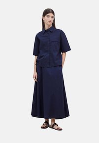 Camisa de color azul marino con mangas cortas y botones en la parte delantera, combinada con una falda larga y fluida. Textura suave, diseño minimalista y sin patrones visibles.