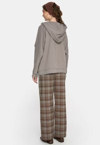 Jasnoszara bluza z kapturem z prążkowanym obszyciem w połączeniu z brązowymi szerokimi spodniami w kratę. Strój cechuje się luźnym krojem i miękką fakturą.