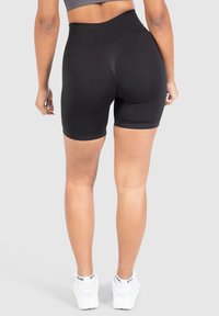 Černé kraťasy s vysokým pasem ze strečové tkaniny, s texturovanými detaily, těsným střihem a hladkým páskem. Kombinované s bílými teniskami.
