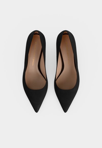 Paire d'escarpins noirs à bout pointu vue de dessus sur fond blanc uni.