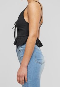 Black ribbed tank top with a peplum hem, featuring thin straps and a tie front. Paired with light blue denim jeans that have pockets.
