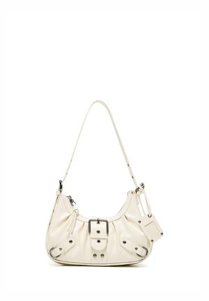 Malá krémová kožená taška cez rameno s detailom prackou, zapínaním na zips, nastaviteľným remienkom a pripevnenou obdĺžnikovou značkou na bielom pozadí.