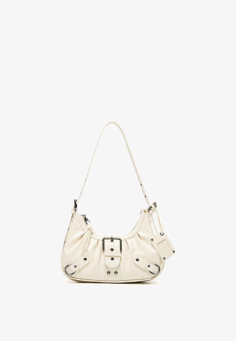 Kleine cremefarbene Lederschultertasche mit Schnallendetail, Reißverschluss, verstellbarem Riemen und angebrachtem rechteckigem Anhänger vor weißem Hintergrund.