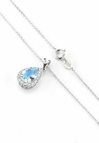 Ogrlica s privjeskom u obliku suze koja sadrži svijetloplavi dragulj okružen prozirnim kamenčićima, na srebrnom lancu s kopčom na školjku.