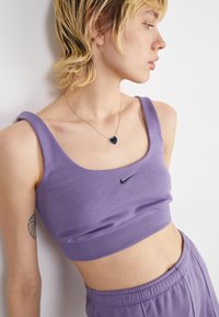 Purple sports bralette made of soft fabric with a scoop neckline and wide straps. Features a black Nike logo on the front.