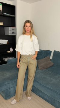 Calças largas bege com cintura ajustável por cordão e t-shirt branca oversized; em pé num sofá de veludo cotelê azul, contra uma parede clara.