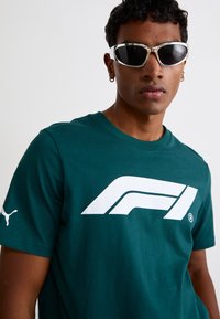 Mørkegrøn bomulds-t-shirt med korte ærmer og et stort hvidt F1-logo på forsiden; har et lille hvidt Puma-logo på ærmet.