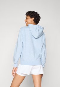 Hoodie azzurro chiaro con una texture morbida, tasca frontale e cappuccio. Polsini e orlo a coste con una vestibilità rilassata, abbinato a pantaloni corti bianchi.