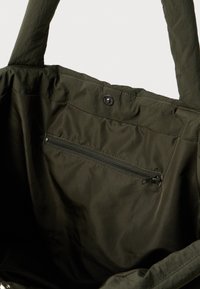 Mørk grønn tote bag indvendig med en glidelås lomme og trykk-knapp lukking nær øverste kant.