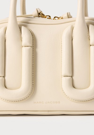 Sac à main en cuir couleur crème avec poignées rembourrées et une fermeture éclair dorée, présentant un logo "Marc Jacobs" subtilement embossé.
