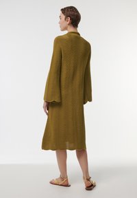 Robe moutarde jusqu'aux genoux avec un motif texturé en vagues, de longues manches cloche et une coupe décontractée. Assortie avec des sandales plates marron clair.