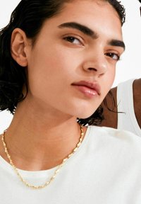 Kullast kett-kaelakee, millel on tekstureeritud lingid, kantud valge särke peal, kaelapiirkonna lähivaade ja osaline vaade inimesest.