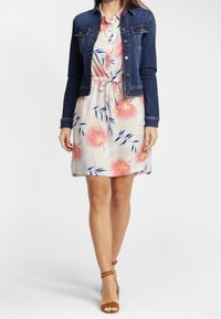 Chaqueta de mezclilla sobre un vestido floral con patrones en rosa y azul. El vestido tiene una cintura con cordón y mangas cortas. Sandalias de tiras color tostado.