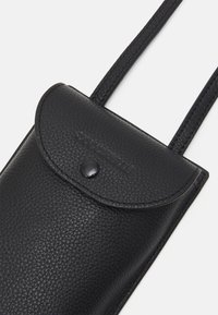 Černá texturovaná kožená taška přes rameno s klopou a zapínáním na patentku, se vzorovaným názvem značky a úzkými ramenními popruhy.