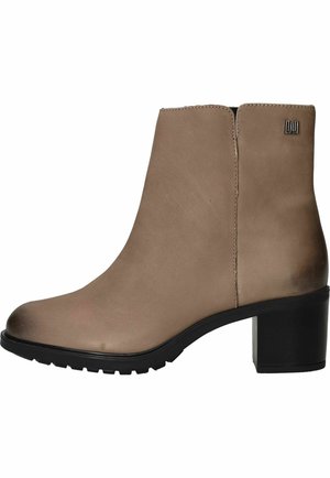 Taupe enkellaarsje met blokhak en robuuste zwarte zool, met een klein metalen logo nabij de bovenrand aan de buitenzijde.