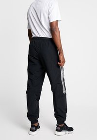 Svarta träningsoverallsbyxor med smal passform, med vita sidostråk, elastisk midja och avskurna fållar. Designade för komfort och rörlighet.