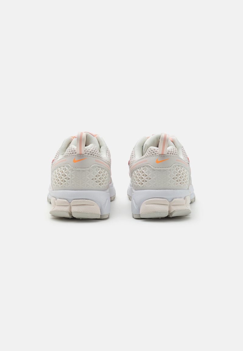 Witte sportieve schoenen met een bovenwerk van mesh met een diamanten patroon, roze accenten en een grijze buitenzool met textuurdetails. Nike-logo op de hiel.